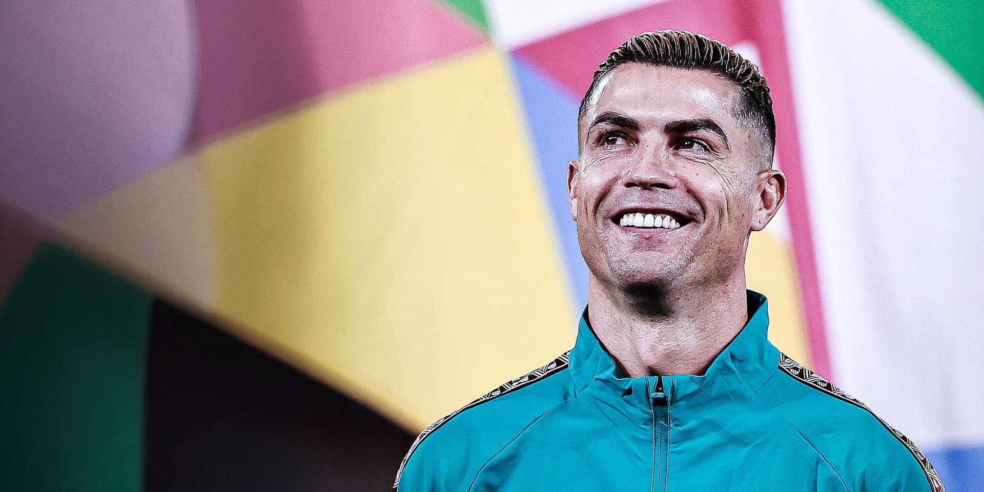 Cristiano Ronaldo lächelt zufrieden im türkisgrünen Trainingsanzug und blickt leicht nach oben vor buntem Hintergrund.