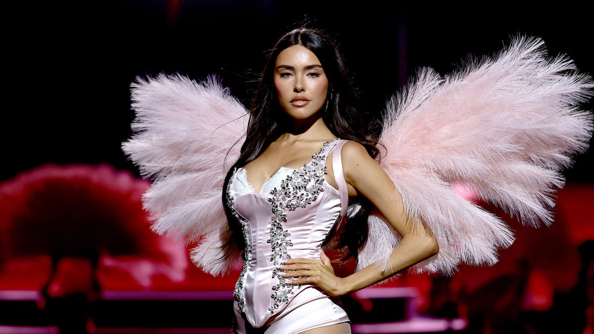 Madison Beer singing into a microphone while walking on a runway during a fashion show.