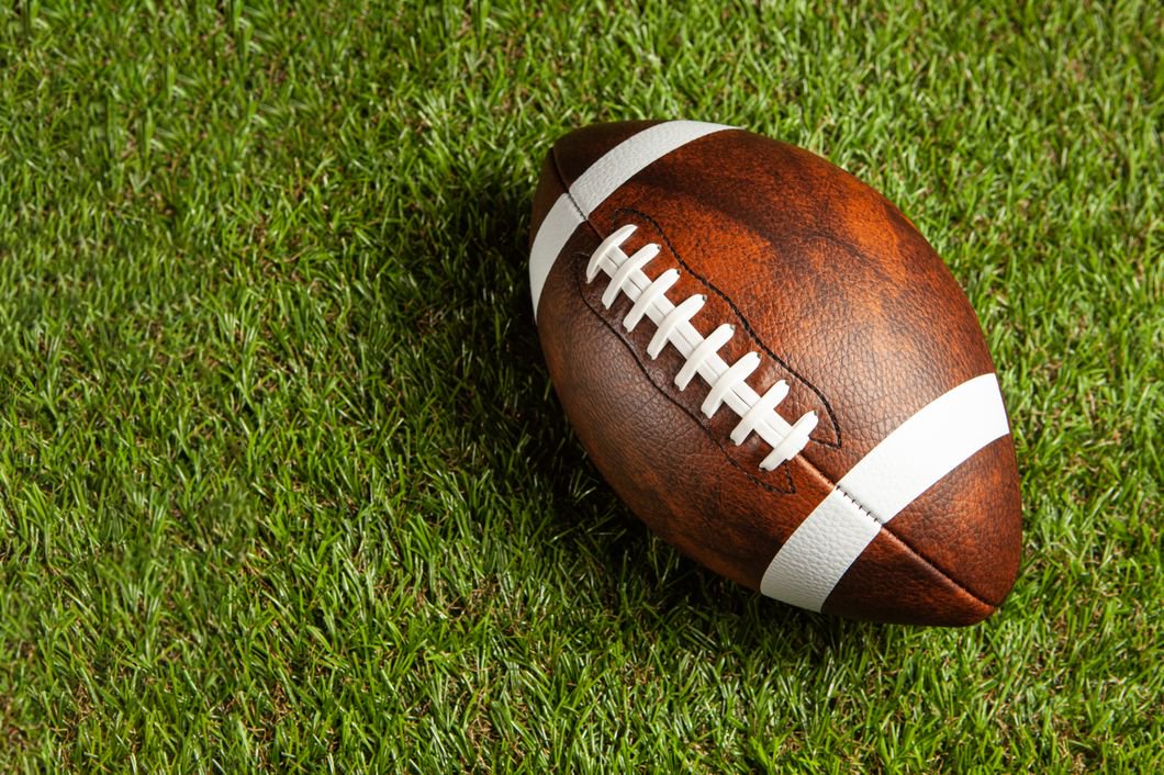 American football ball on green grass field background.
