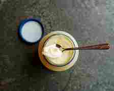 Jar of yogurt with spoon, on a dark surface, next to open lid
