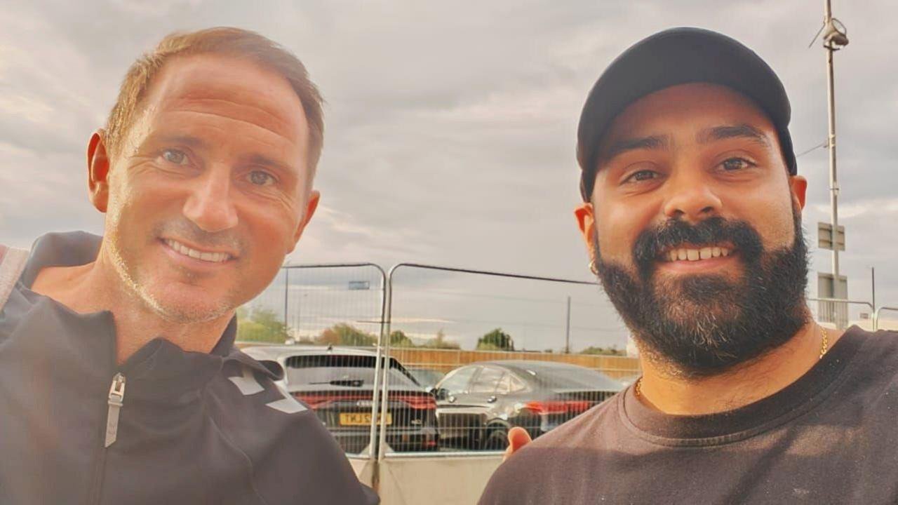 A selfie of Parmdip Dhillon on the right, who has long black facial hair and is wearing a black cap and t-shirt, next to Frank Lampard, who has short light brown hair and is wearing a black windbreaker jacket
