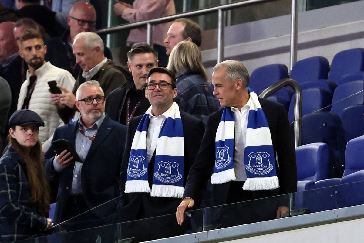 A group of individuals, dressed formally, are gathered on the sidelines of a sports stadium, wearing blue and white striped scarves, and observing the ongoing event from the stands.