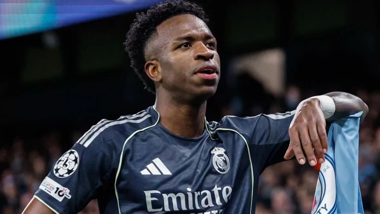 Jogador Vini Jr. de camisa Real Madrid, patches, "Emirate", braço em camisa Manchester City
