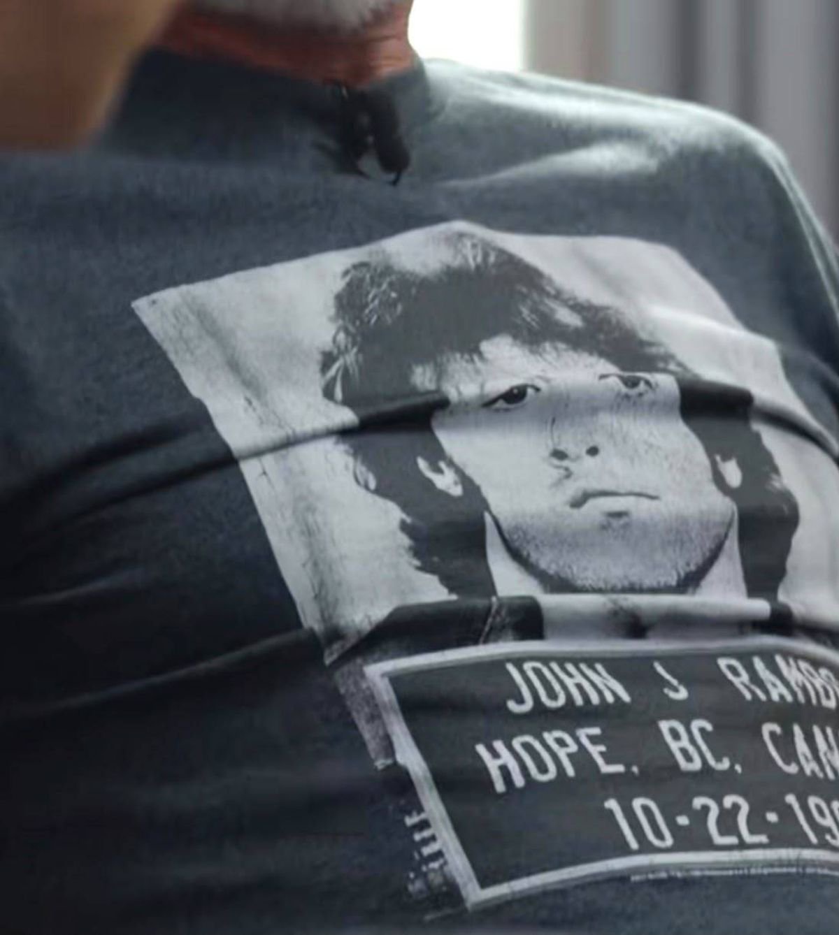 A close-up view of a black fabric with a printed image of a person's face and the text "John J. Rambo" in white font.