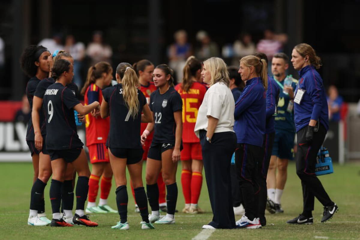 U.S. women's soccer coach Emma Hayes, front in white, stands on field during an international friendly match against Spain.