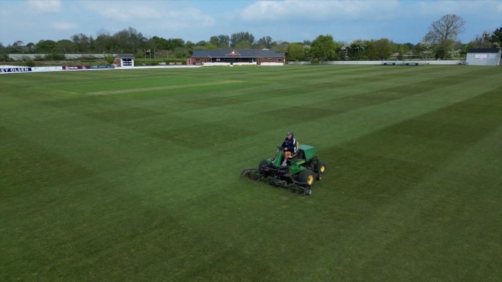Jimmy Perchard on his lawn mower at Farmers field ground with the club house in the background. 