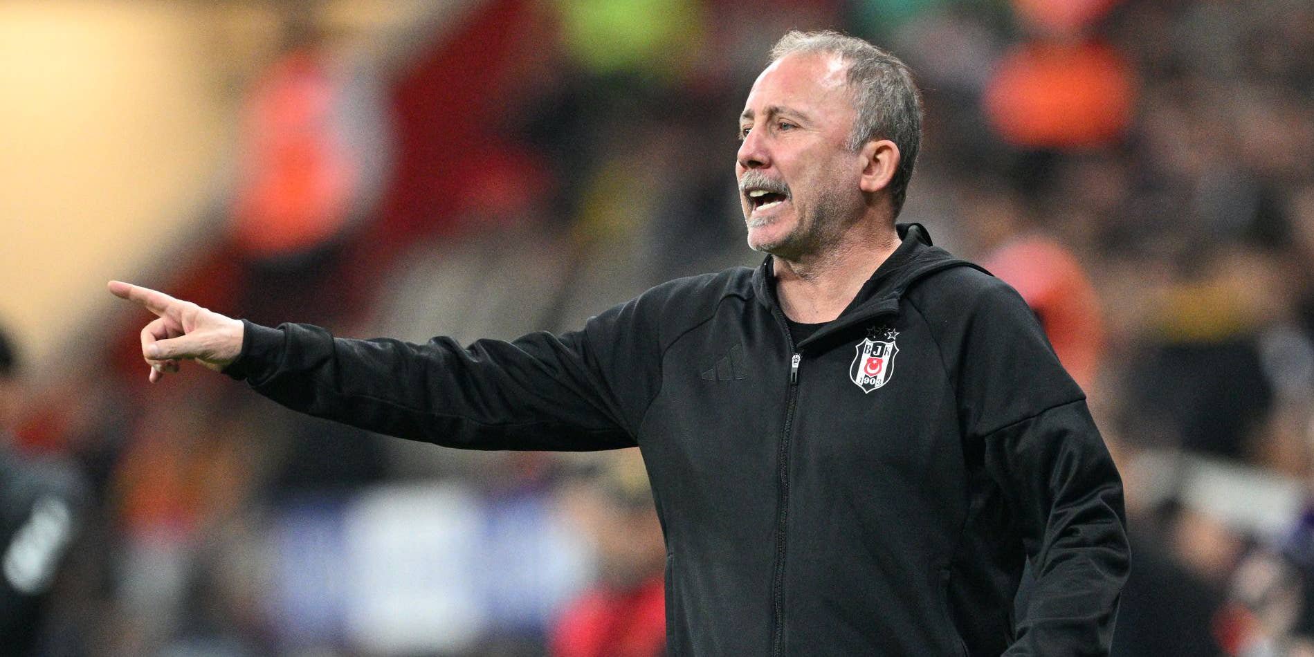 Sergen Yalçın steht in einer schwarzen Trainingsjacke am Spielfeldrand und deutet energisch mit dem Zeigefinger auf das Spielfeld.