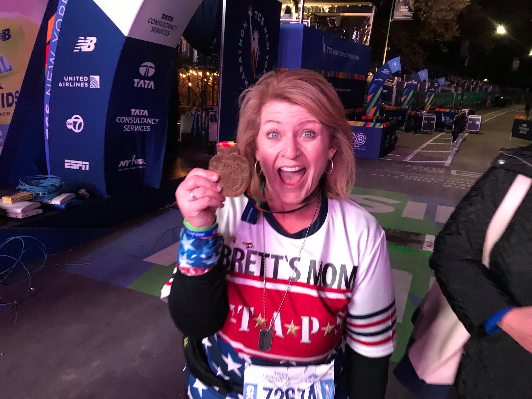 Shellie Warren celebrates at the New York City Marathon finish line, holding her medal.