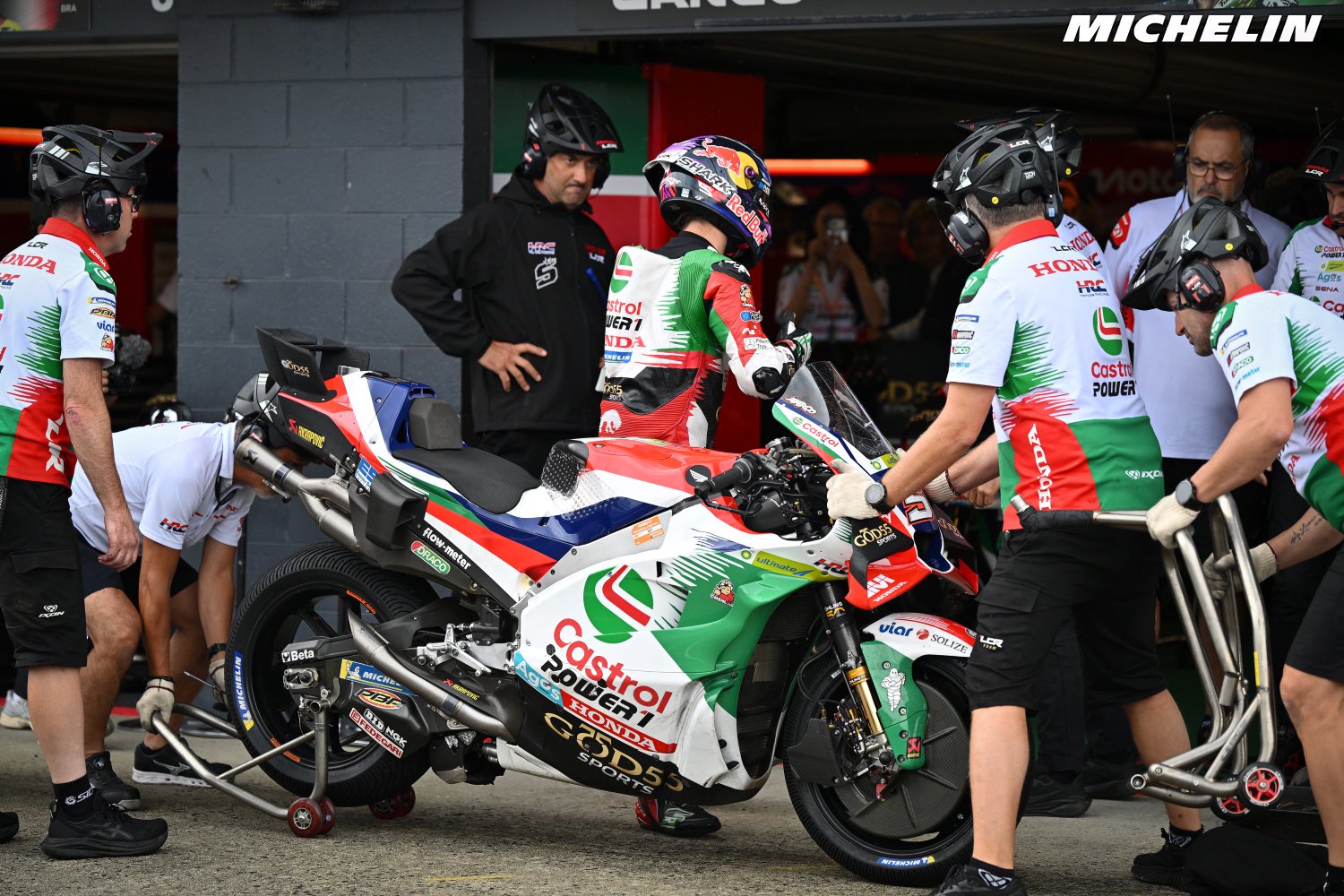 Johann Zarco's LCR Honda being pushed through the pit lane at Phillip Island, rider in Castrol-liveried leathers and helmet, team crew in white and green.
