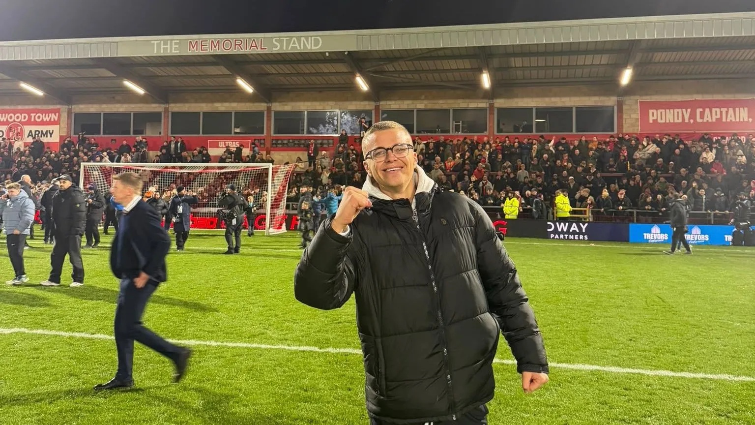 BEN KNAPMAN Ben, a man wearing glasses and with short grey hair, celebrates on the pitch