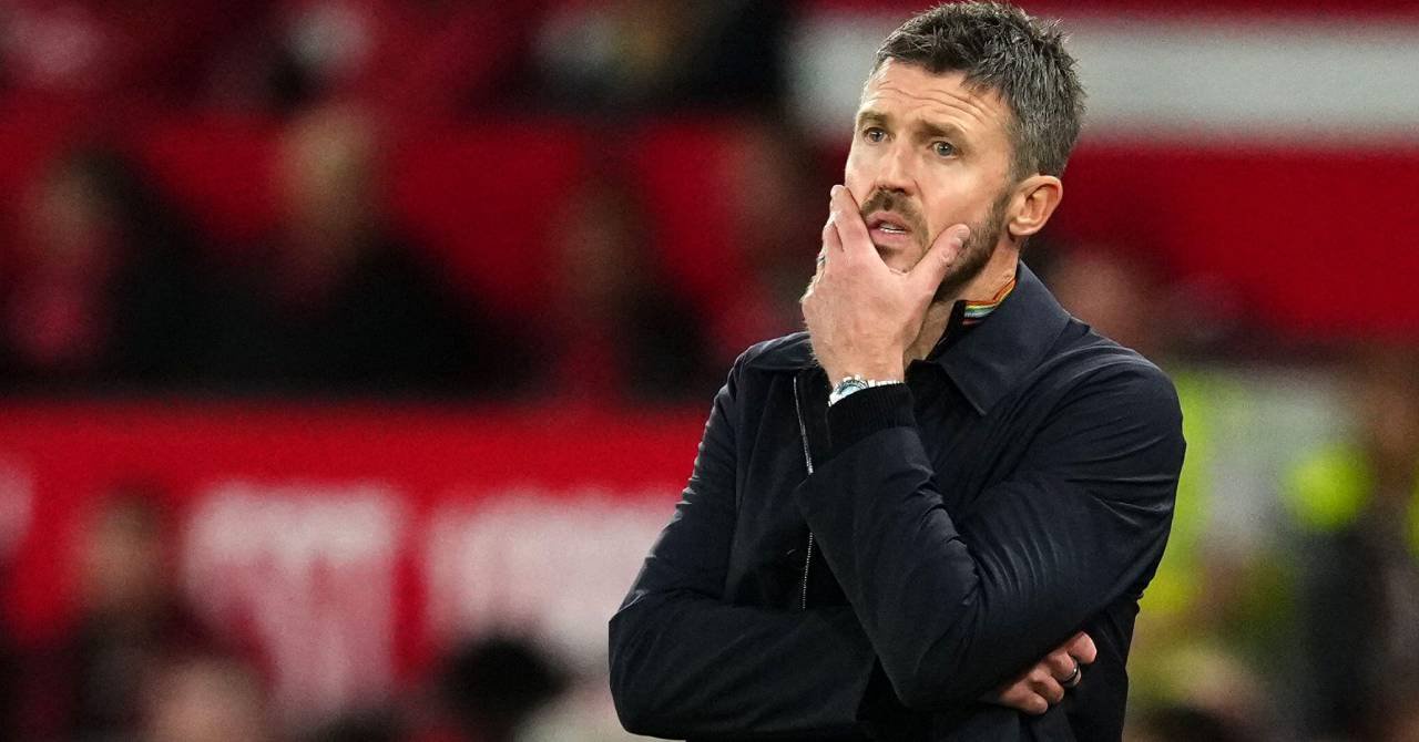 Football manager Michael Carrick looking to his right while holding his left hand to his chin in a stadium in his role as head coach of Premier League team Manchester United Football Club and wearing a black jacket with a watch on his raised arm