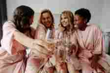 Women celebrate a bachelorette party of bride. Group of female sitting on bed and toasting champagne glasses at home. Focus on champagne flutes.
