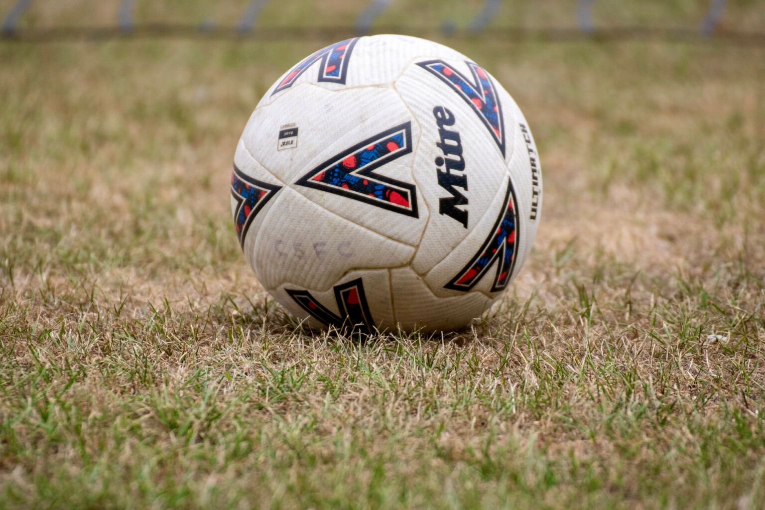 Close-up of a white football resting on worn grass of a pitch