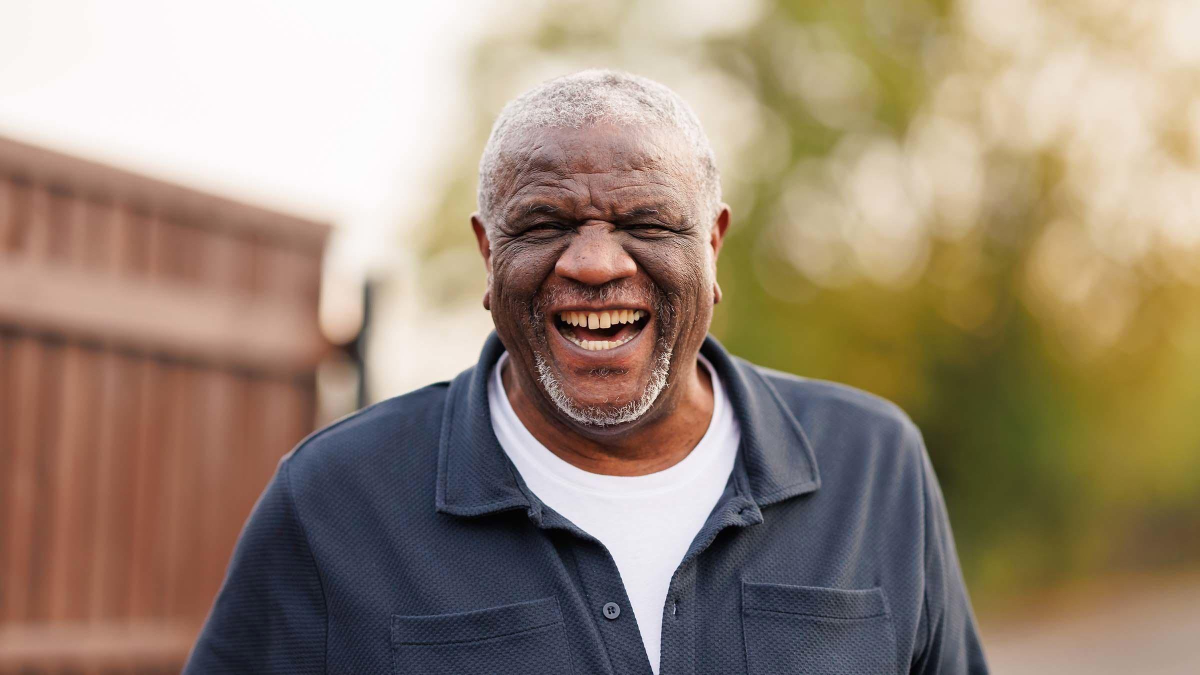 A man in a dark blue shirt over a white T-shirt is smiling widely at the camera