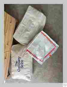 3 closed bags if various materials on the floor beside a nightstand each holding folded bed sheets