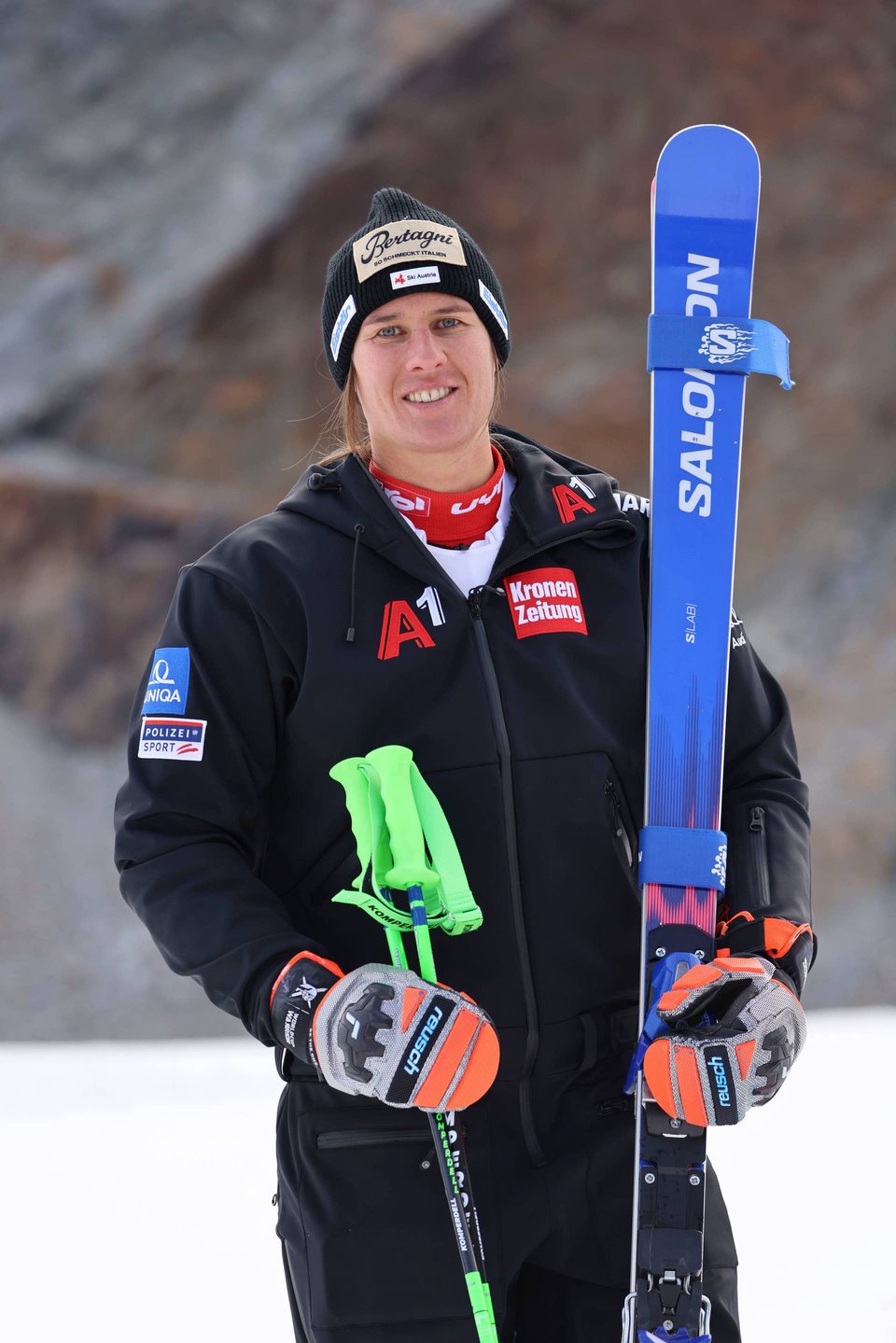 Eine Skifahrerin steht im Schnee mit Skiern und Skistöcken, trägt Winterkleidung und Mütze.