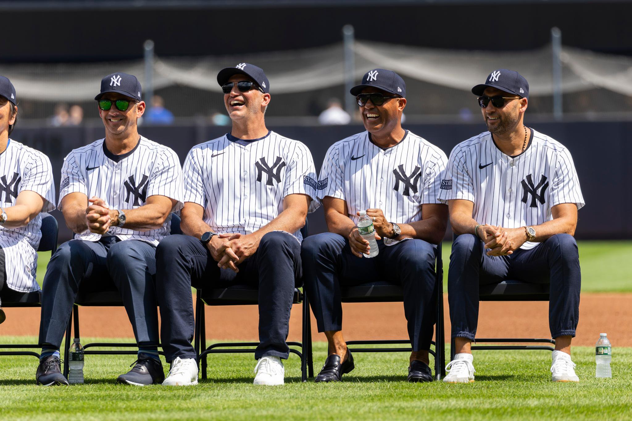 Former New York Yankees players Jorge Posada, Andy Pettitte, Mariano Rivera and Derek Jeter laugh as they sit on the field.