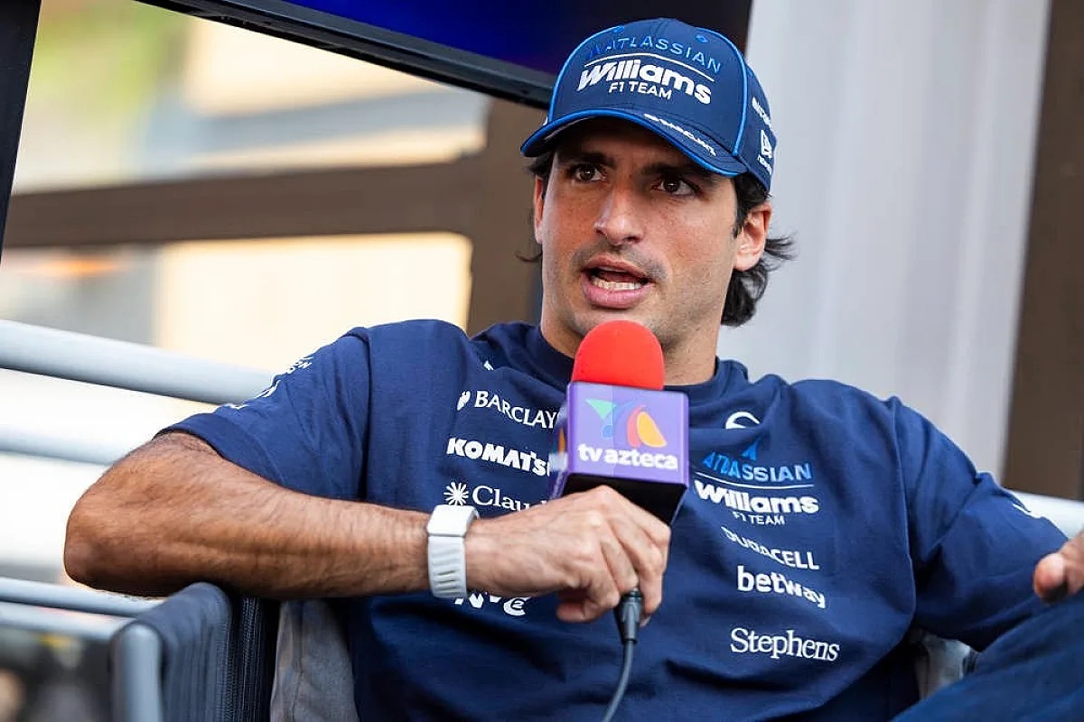 Driver in a navy Williams F1 Team cap and shirt speaking into a TV Azteca microphone at a press event