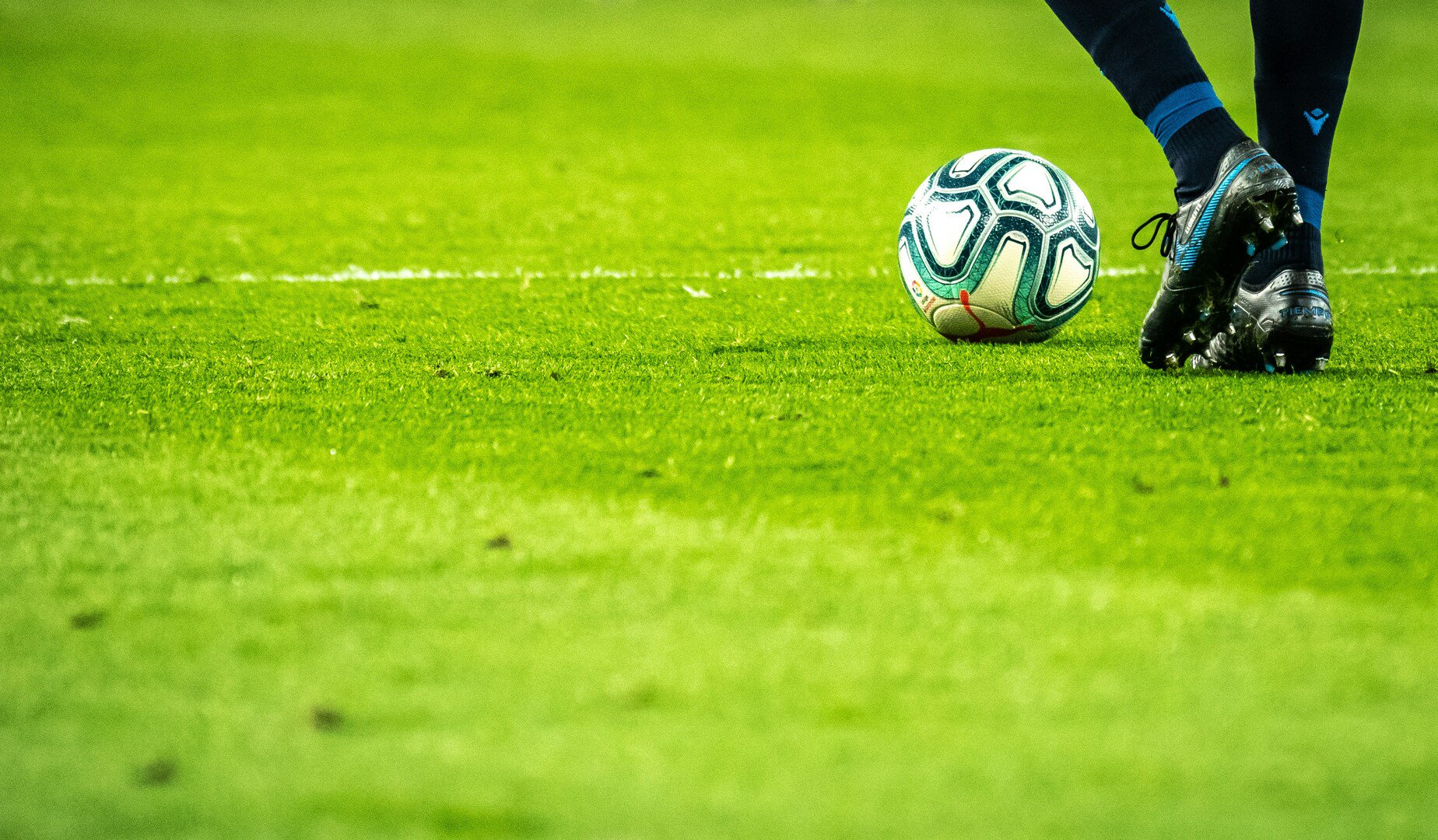 Fußball und Beine mit schwarzen Schuhen und Stutzen auf grünem Rasen