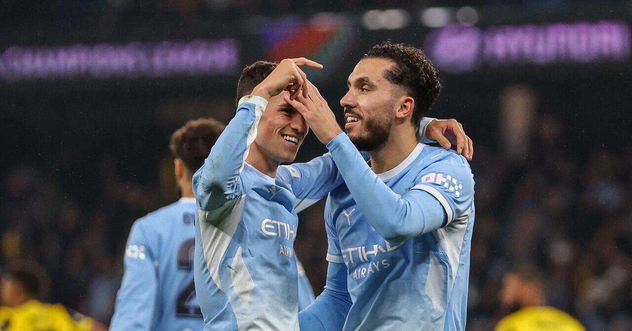 Footballer Phil Foden raising his left arm and putting his left over the shoulder of facing teammate Rayan Cherki while the players smile to celebrate a goal for Premier League team Manchester City Football Club. The pair are wearing light blue shirts with white details and the words Etihad Airways and Puma logos visible on the chest.