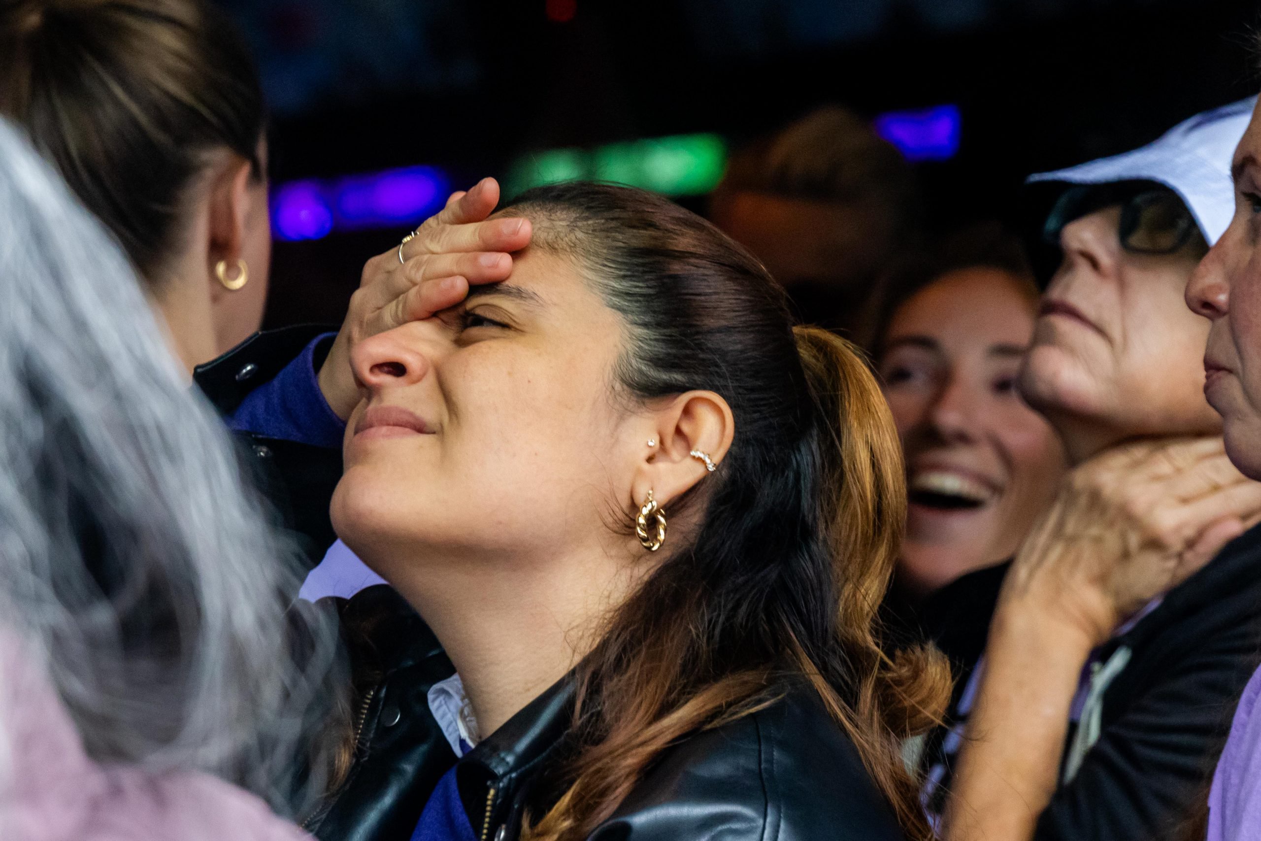 A woman in a crowd with her hand to her forehead, surrounded by other people.