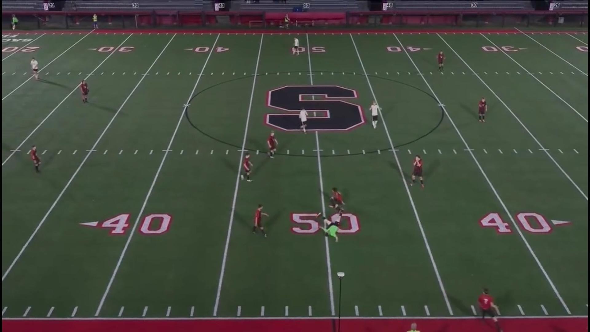 High-angle view of a soccer game in progress on an American football field at night.