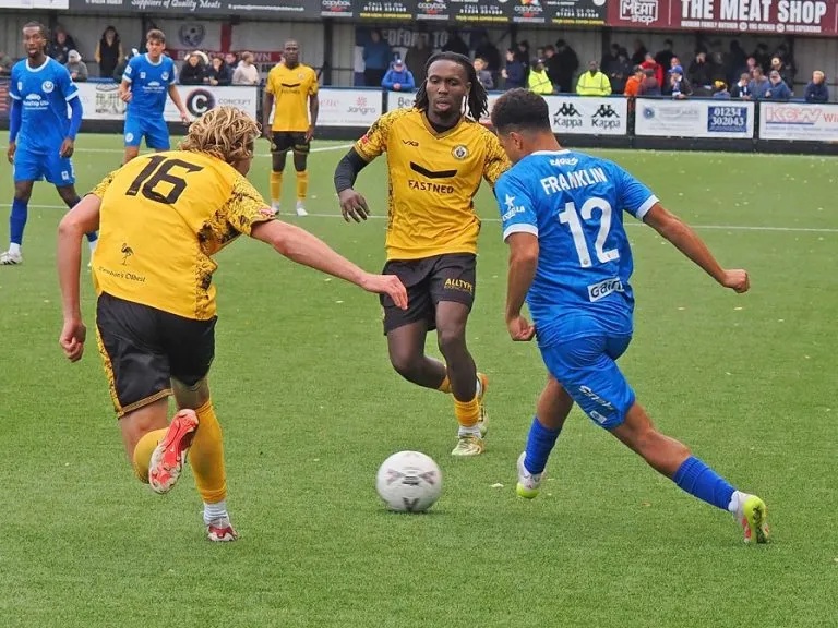 Lewis Franklin of Bedford Town passes the ball between two yellow-shirted Cray Wanderers defenders at The Eyrie