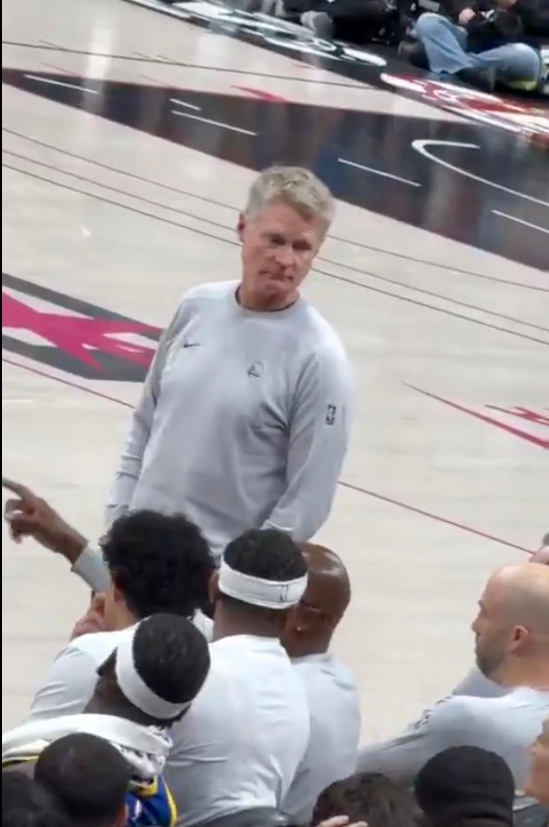 Steve Kerr reacts to a double-ganger drinking a beer in the crowd during a game.