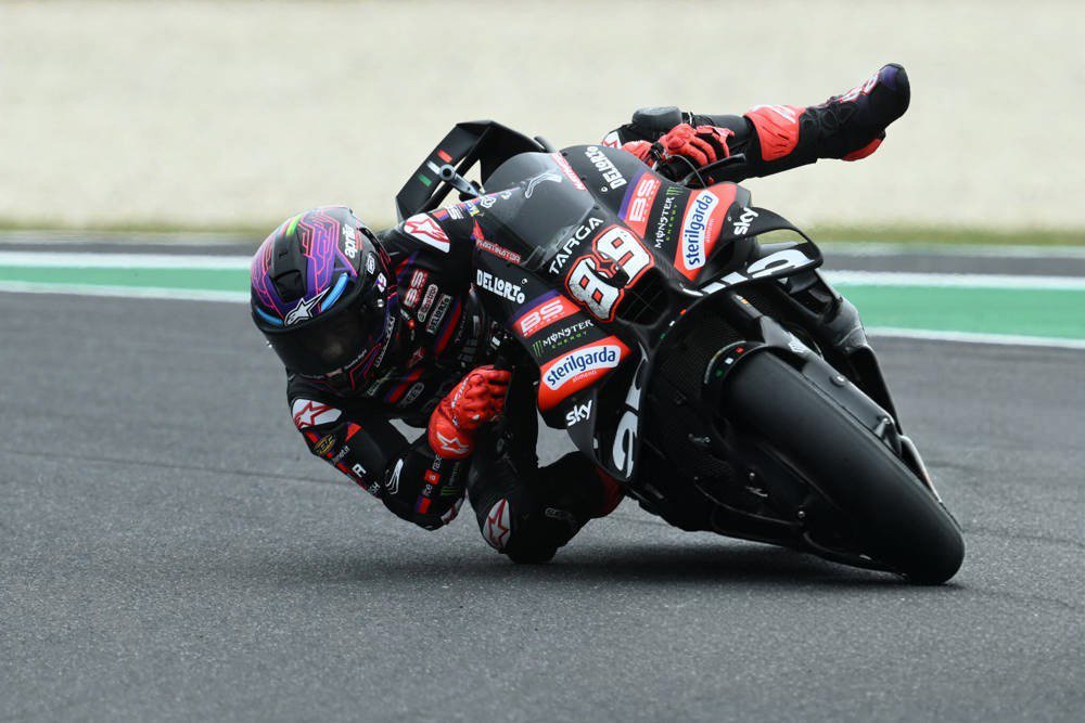 Rider in black and red leathers and helmet leaning deep into a corner on a black Aprilia MotoGP bike, number 89 with Sterilgarda and Sky livery.