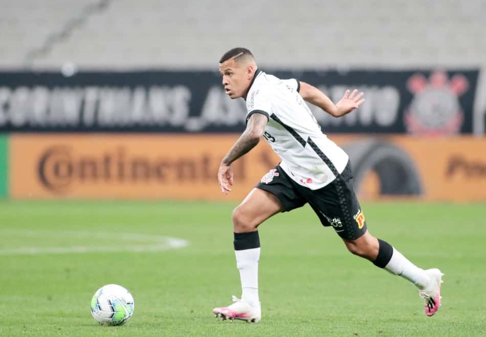 Jogador do Corinthians em uniforme branco e preto corre atrás da bola em campo durante o jogo