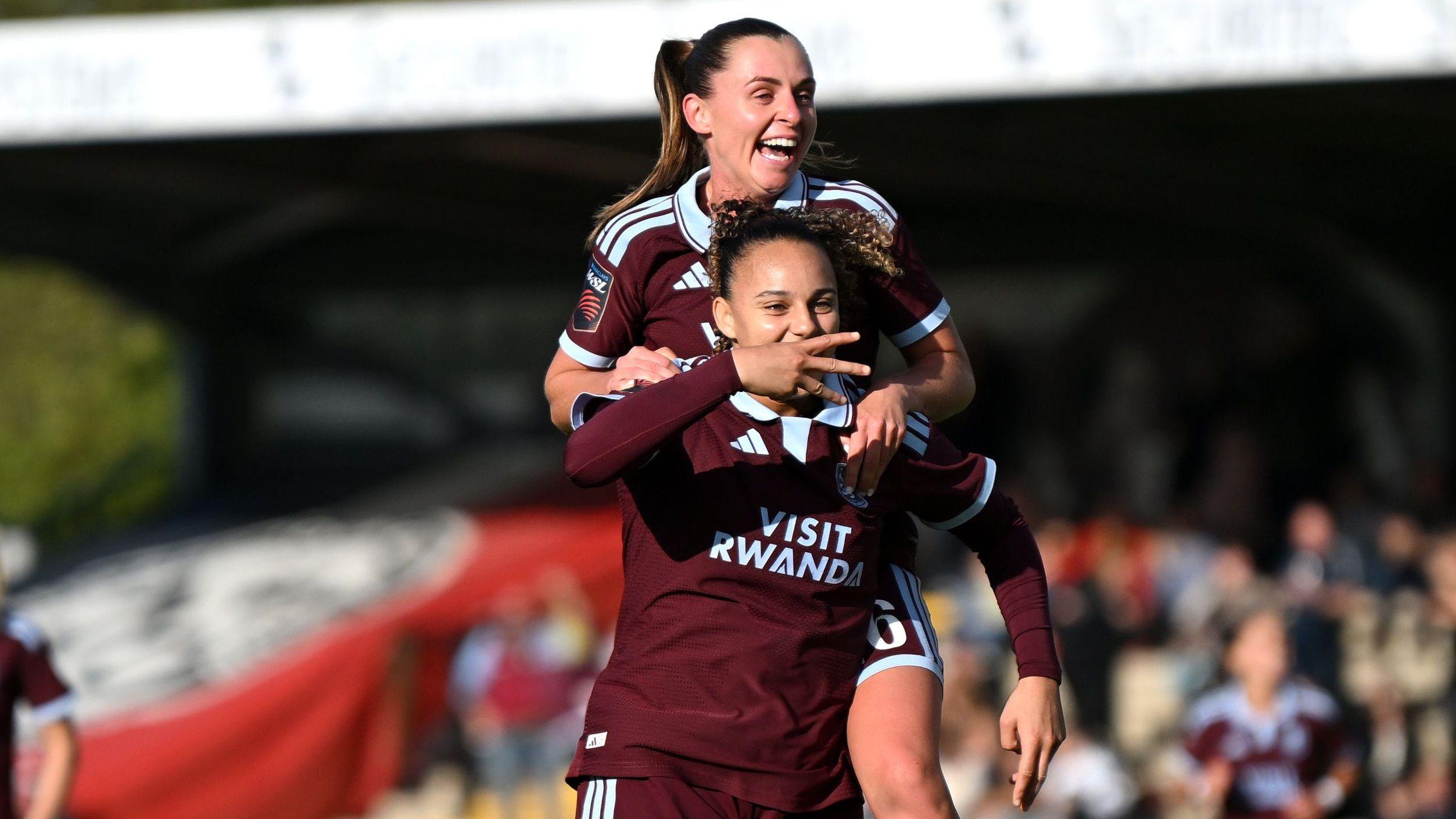 Chasity Grant celebrates her goal for Aston Villa by holding out three fingers sideways while team-mate Noelle Maritz jumps on her back