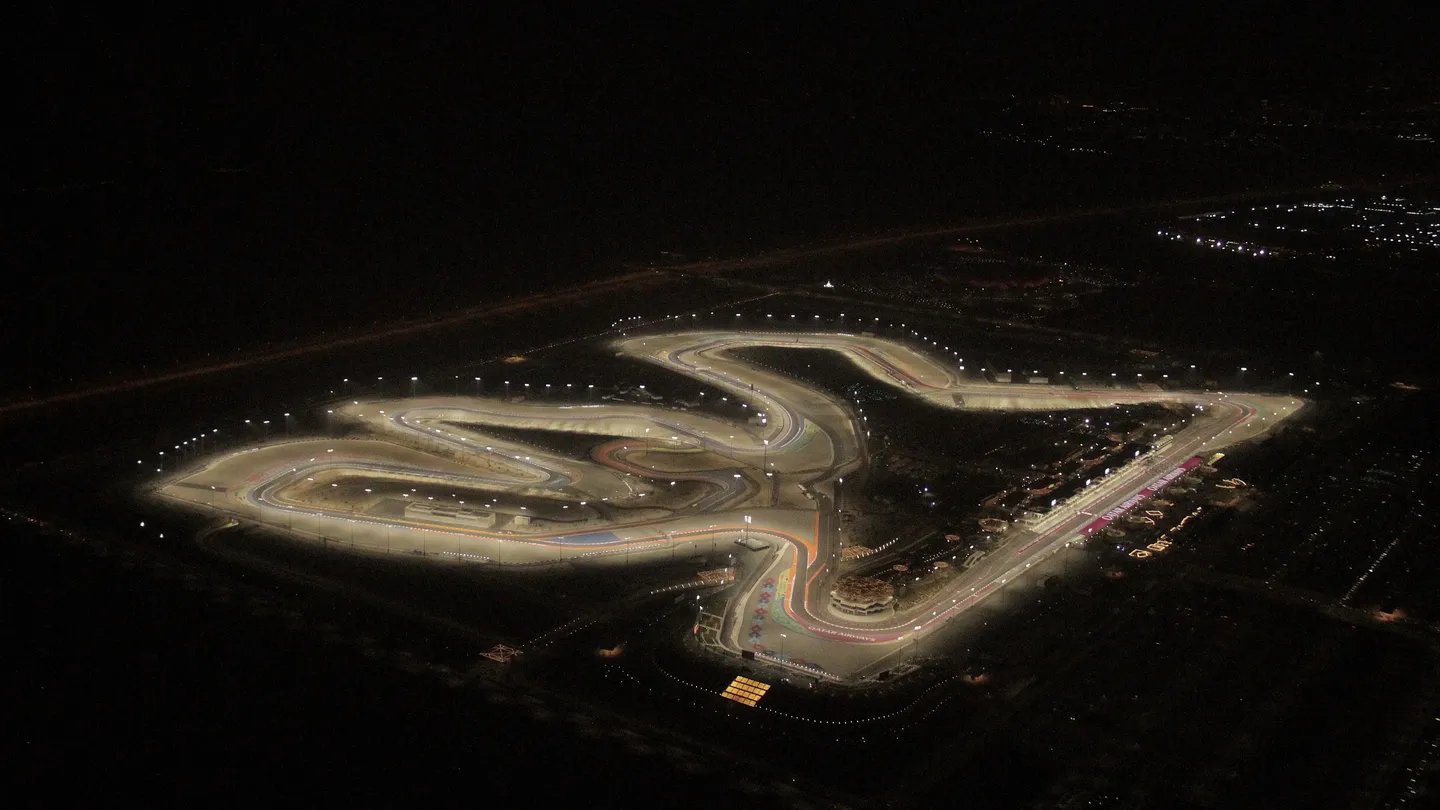 Aerial night view of an illuminated Formula 1 circuit with glowing track lights and grandstands, showing the Losail-style layout used for the Qatar Grand Prix.