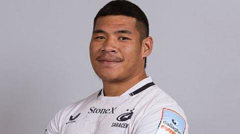 Totoa Auvaa standing for a team issue photo, wearing white Saracens kit looking towards the camera