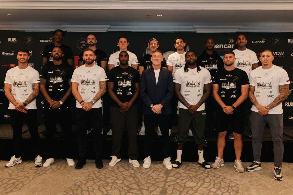 Group photo of fifteen men, including boxers and staff, standing in two rows in front of a branded backdrop.