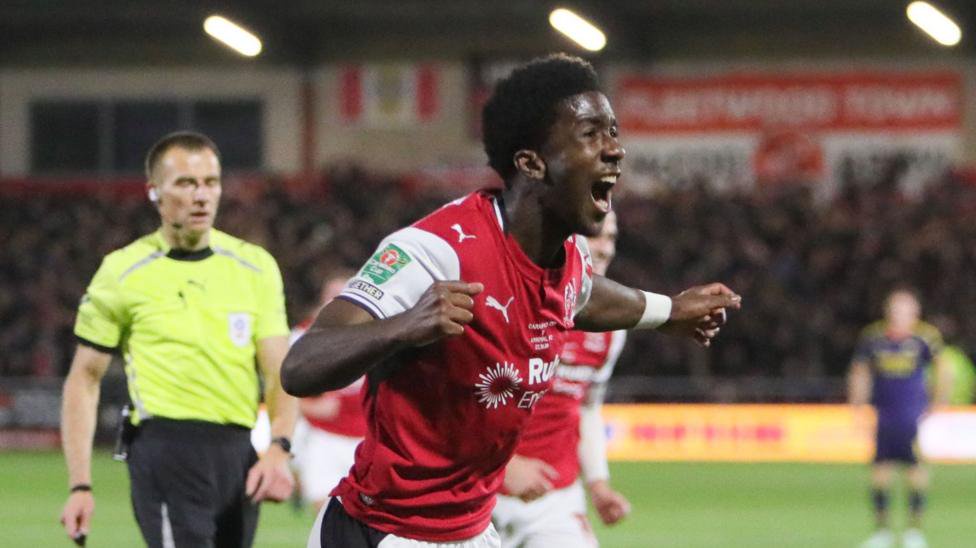 Aaron Loupalo-Bi celebrating scoring for Fleetwood Town against Arsenal in the Carabao Cup, holding his arms out wide with his mouth wide open.