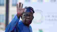 Nigeria President Bola Tinubu, wearing a blue gown and hat, waves as he arrives for the closing session of the New Global Financial Pact Summit, on June 23, 2023 in Paris