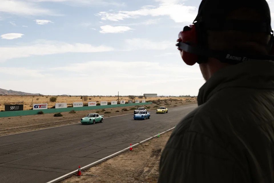 A person watches cars racing on a track in a dry landscape, with various car colors visible in the scene.