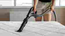 Woman wearing beige shorts vacuuming her white mattress to get rid of bed bugs
