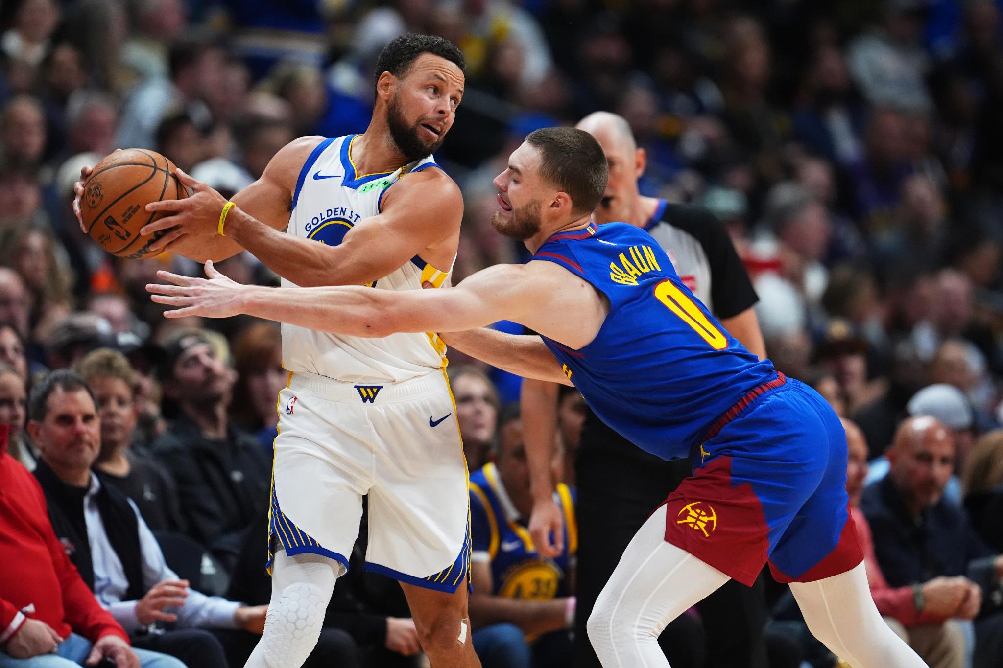 Golden State Warriors guard Stephen Curry holds the ball while under defensive pressure from Denver Nuggets guard Christian Braun during an NBA game.