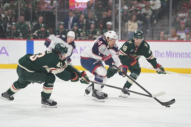 Columbus Blue Jackets left wing Ryan Lomberg (94) skates with the puck as Minnesota Wild defensemen Quinn Hughes, left, and Daemon Hunt, right, defend during the first period of an NHL hockey game, Sunday, Oct. 18, 2026, in St. Paul, Minn. (AP Photo/Abbie Parr)