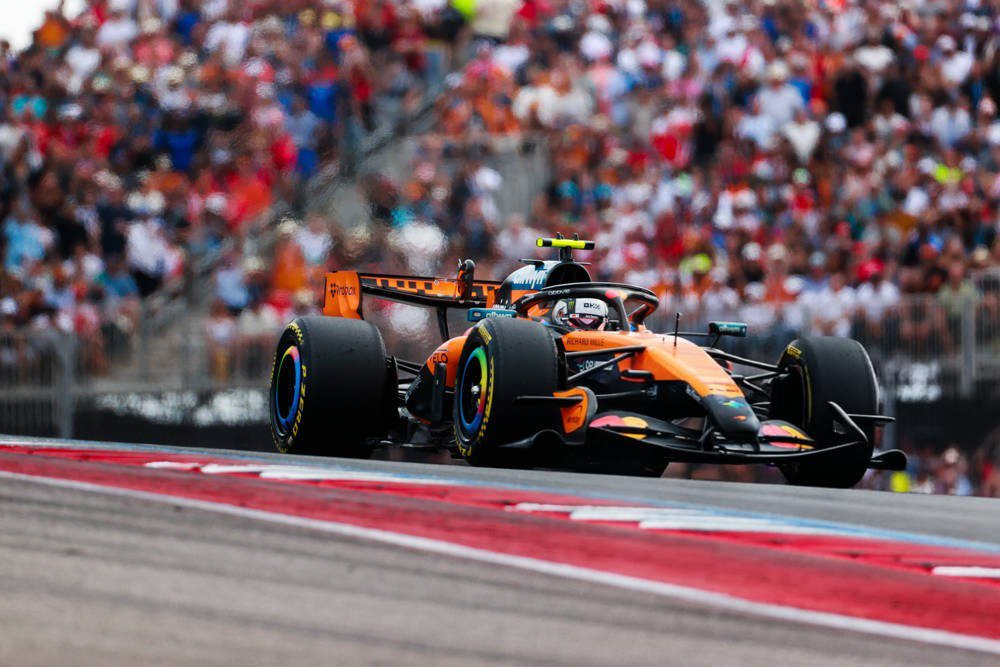 Lando Norris in his orange McLaren Formula 1 car on track at the United States Grand Prix, with crowded grandstands behind
