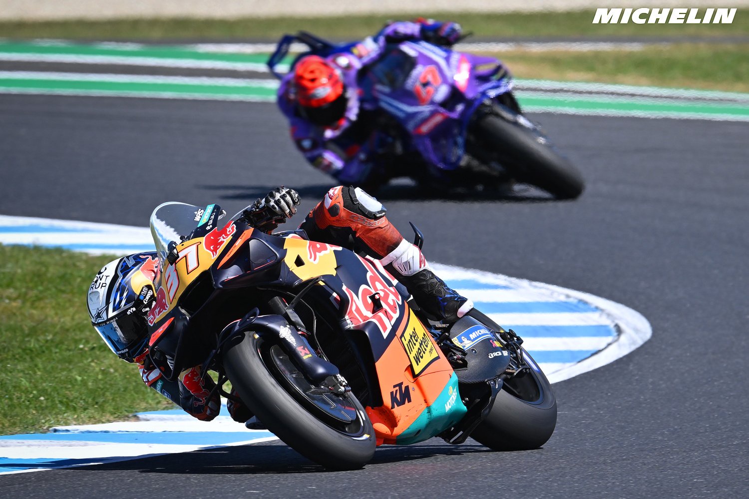 Pedro Acosta on his Red Bull KTM MotoGP bike leaning into a corner at Phillip Island, with a Michelin logo and rival rider behind
