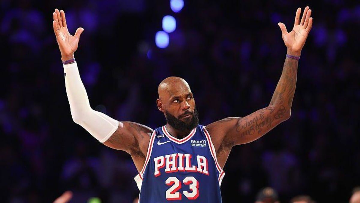 Lebron James, wearing a blue vest with Phila 23 in white text, holds his arms in the air