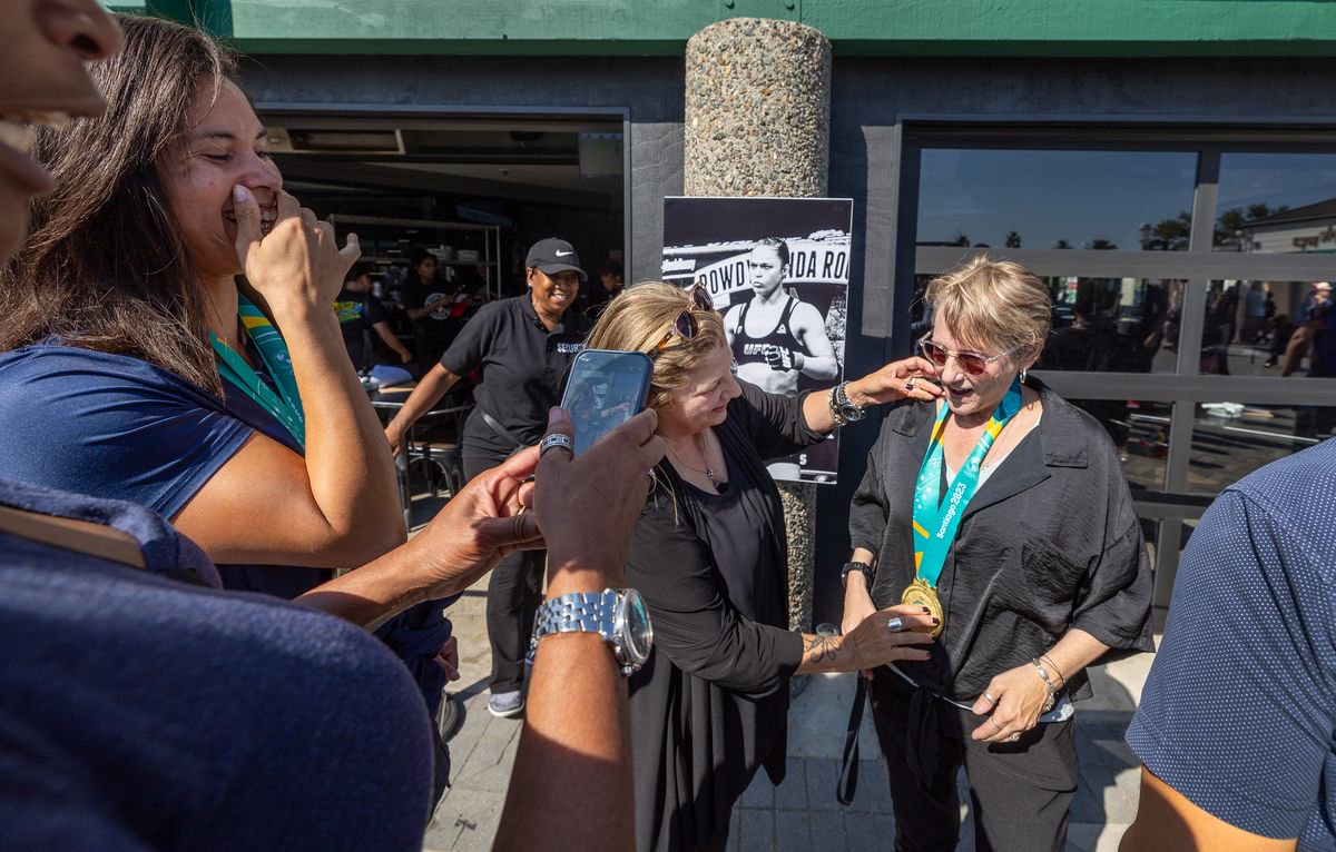 Watch Me! Sports Bar Co-owners Emme Eddy, center, places Olympic medals from rower Maddy Focht, left, of Long Beach, on Jax Diener, right center, during the grand opening in Long Beach Friday, July 26, 2024