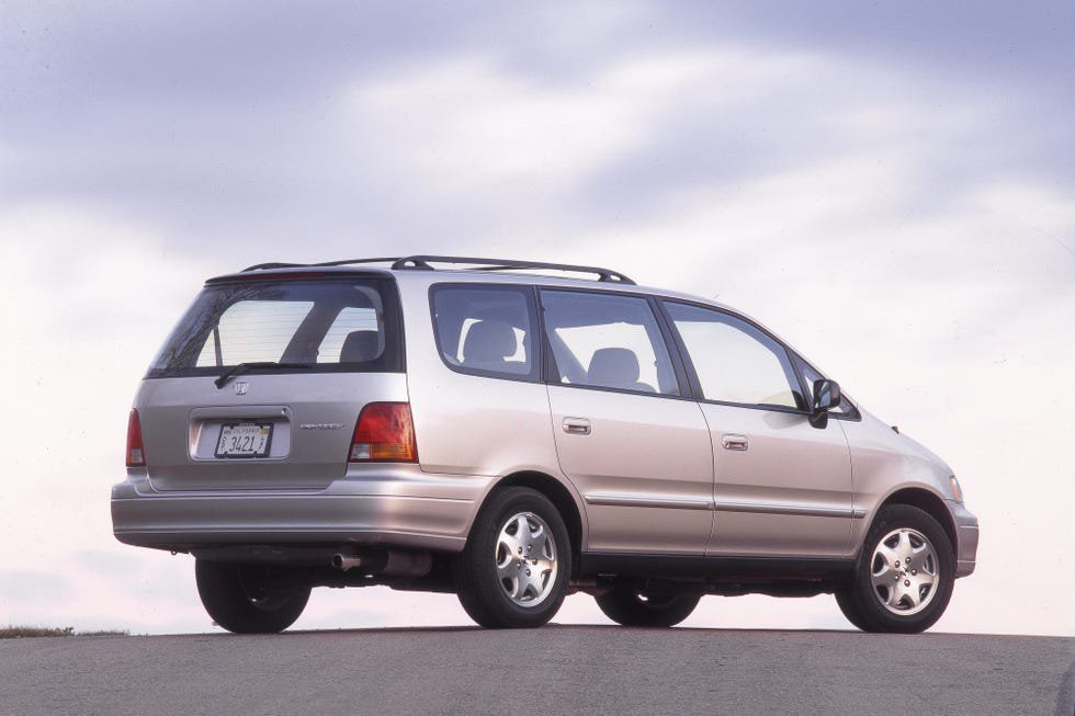 A silver Honda Odyssey minivan parked along a scenic road under a cloudy sky.
