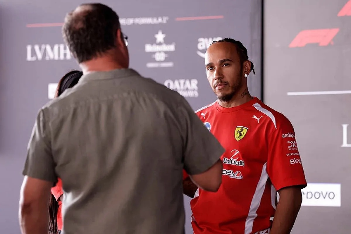 A Ferrari-liveried F1 driver in a red Puma shirt speaks with a man in a grey shirt at a Formula 1 event backdrop