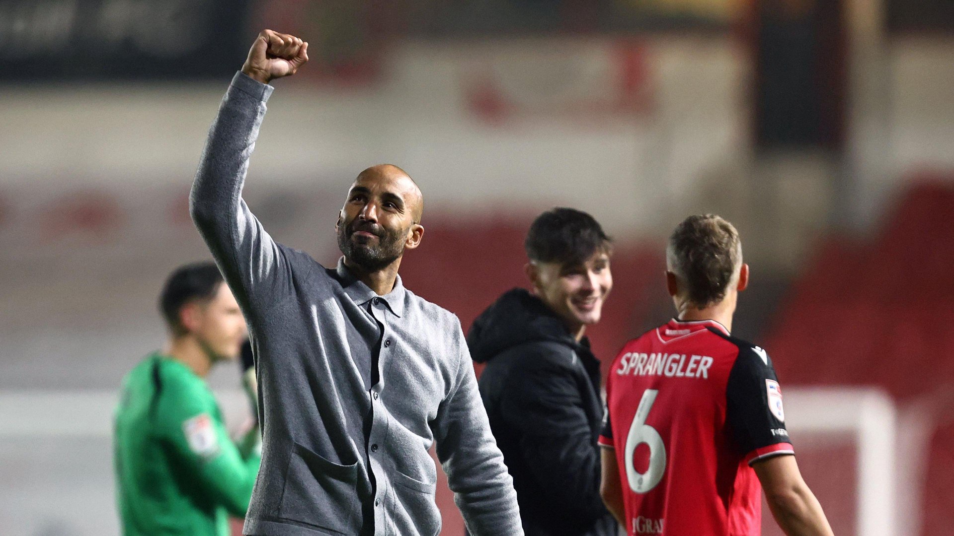 Lee Grant raises a fist in celebration towards Walsall fans. He is wearing a grey top while Walsall players are talking in the background