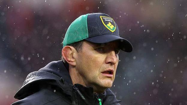 Northampton Saints director of rugby Phil Dowson wearing a black and green Northampton Saints cap looking on in the rain prior to his side's match against Leicester Tigers.
