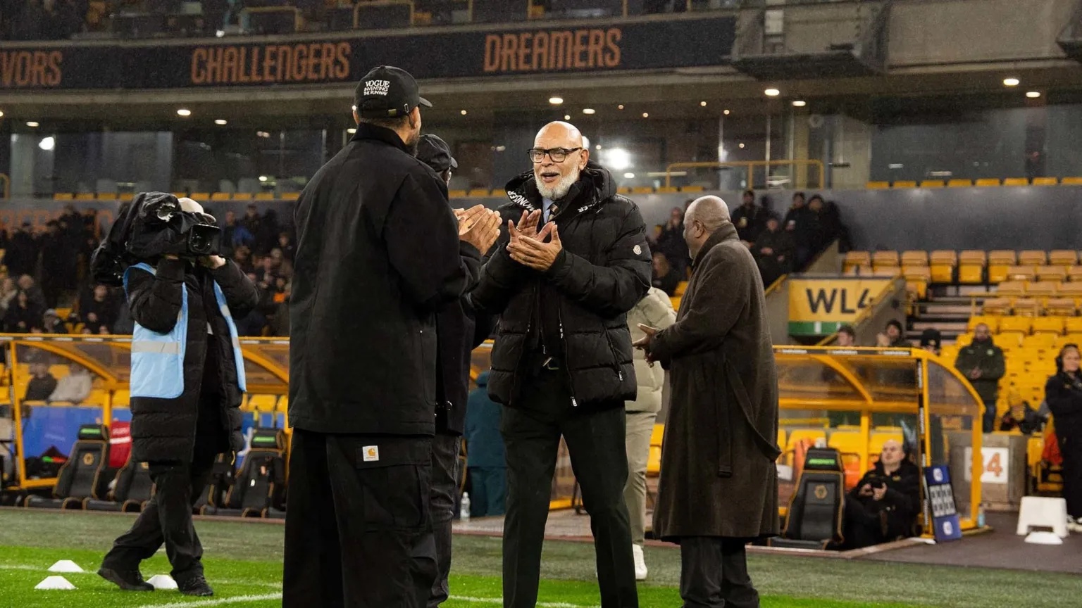 Wolverhampton Wanderers A group fo men in black coats are standing on a footbal pitch 