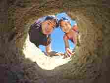A man and a young girl smile as they look down into a hole in the ground, viewed from the bottom looking up